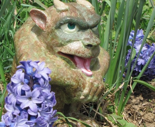 Photo of a gargoyle statue sitting next to purple hyacinths.